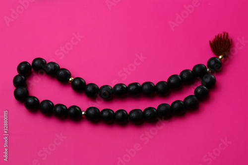 Photography Black wooden rosary in on a pink background
