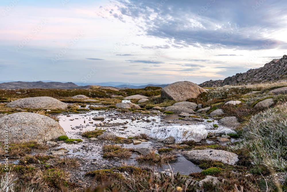 Moody evening close-up shot of an alpine pond with grass details and a white rock near the summit of Mount Kosciuszko (2228m above sea level) in Kosciuszko National Park, New South Wales, Australia.