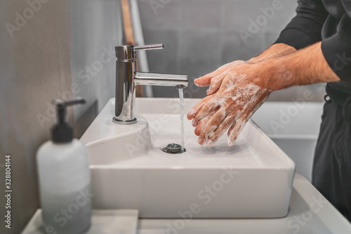 Washing hands with soap and hot water at home bathroom sink man cleansing hand hygiene for coronavirus outbreak prevention. Corona Virus pandemic protection by washing hands frequently. photo