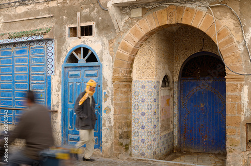 Passersby and blue doors in Essaouira Medina with ornate stonework and Zellige tilework © Reimar