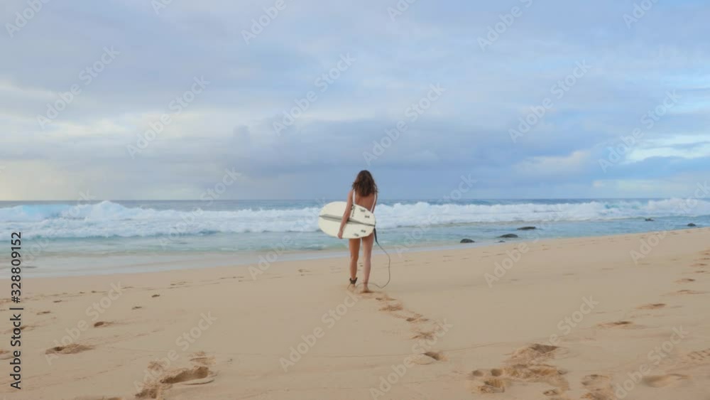 Surfer walks by rocks at Hawaiian beach, looking around for good waves, readiness for a surfing session Surfer walks by rocks at Hawaiian beach, looking around for good waves, readiness for a surfing session