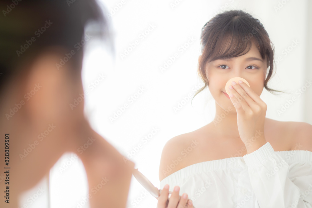 Portrait beautiful young asian woman applying powder puff at cheek makeup of cosmetic looking mirror, beauty of girl with skin face smile in the bedroom, health and wellness concept. Portrait beautiful young asian woman applying powder puff at cheek makeup of cosmetic looking mirror, beauty of girl with skin face smile in the bedroom, health and wellness concept.