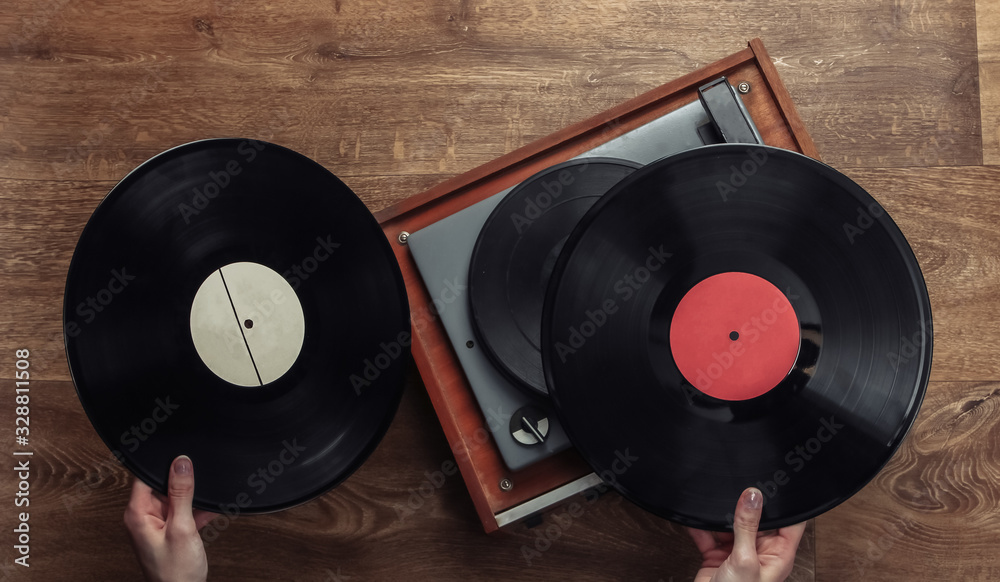 Fototapeta premium Female hands pick up vinyl record for vinyl player on a wooden floor. Music lover, 70s, top view, nostalgia