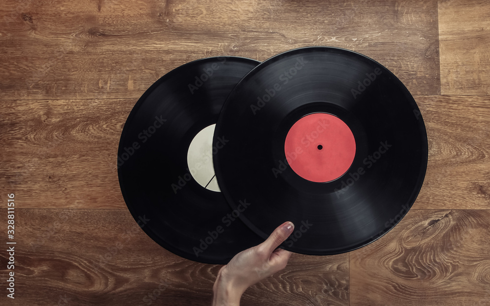 Obraz premium Female hand holds two vinyl records on a wooden floor. Top view