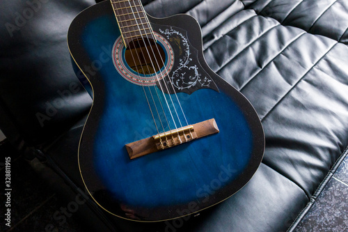 A wooden blue guitar lies on a black sofa