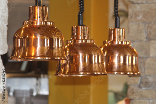Three shinny light shades in a row over a meal counter in a pubs restaurant. Retro lighting decor over a servery. The lamps are copper colour. photo