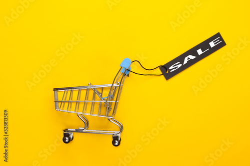 Mini shopping trolley with black sale tag on yellow background. Top view. Discount. Minimalism