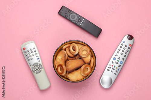 TV remote control and bowl of crackers on a pink pastel background. Watching the TV. The concept of home rest after work. Top view. photo