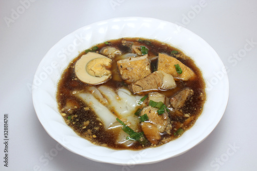 Chinese roll noodle soup (Guay Jub Nam Kon call in Thai) with crunchy pork, egg and cinnamon in white bowl on white background, it’s one of the top Thai street food dishes to try