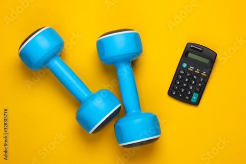 Fitness, sport concept. Calorie Counting. Calculator and dumbbell on a yellow background. Top view