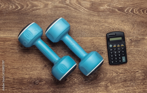 Fitness, sport concept. Calorie Counting. Calculator and dumbbell on wooden floor. Top view