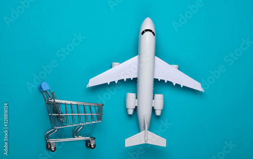 Flat lay composition. Air delivery, shopping, logistics. Figurine of shopping trolley, airplane on blue background. Top view