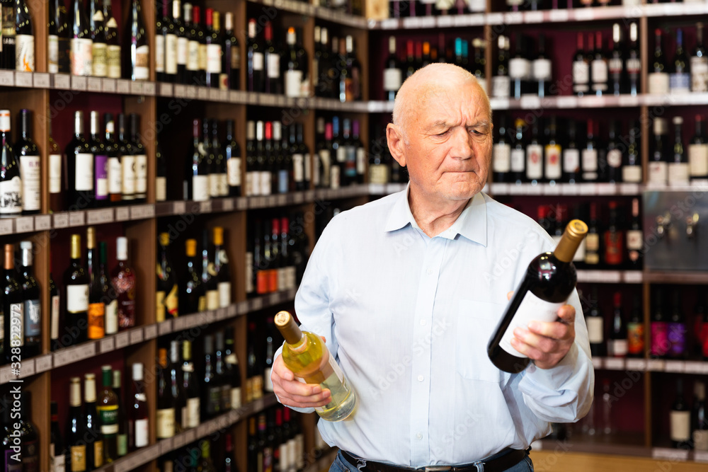 Serious retiree chooses white and red wine in a liquor store