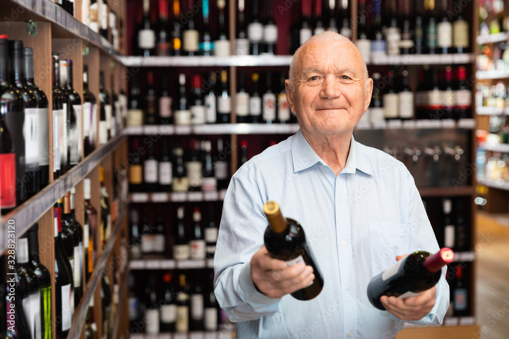 Happy smiling mature man customer choosing bottles of wine in wine store