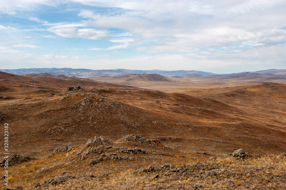 Beautiful steppe landscape with hills and stones in brown tones. Alien landscape. Clouds in the sky.