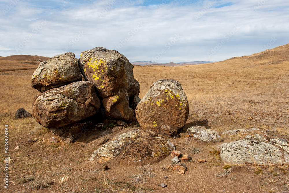 Large boulders in the steppe. The hills are behind. The sky with clouds. Brown tones.