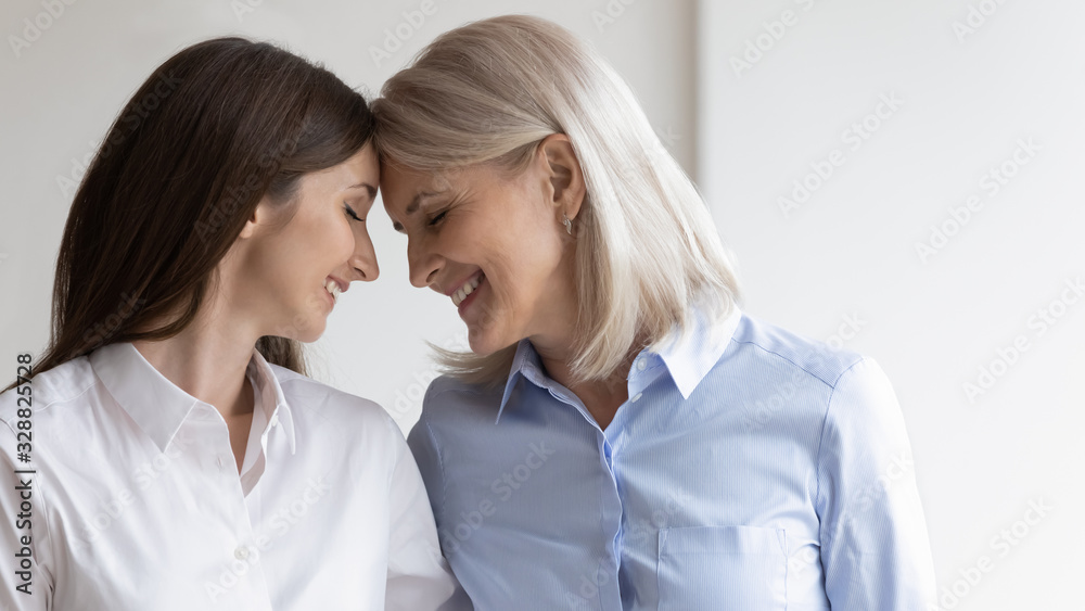 Happy senior mother and adult daughter touch foreheads hug cuddle show love and care, smiling mature mom and grown-up girl enjoy tender close moment at home together, family bonding concept