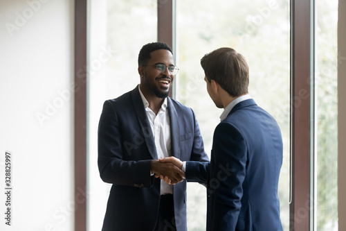 Overjoyed multiethnic businessmen shake hands greeting getting acquainted in office, smiling diverse multiracial male business partners handshake close deal make agreement after successful negotiation photo