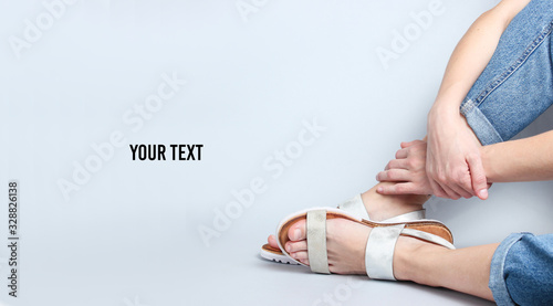Female legs in jeans and trendy sandals sitting on white background. Cropped Studio Shot. Copy space