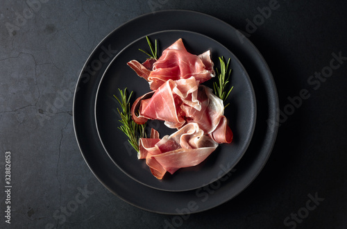 Fotografie Prosciutto and rosemary on a black plate. Top view.