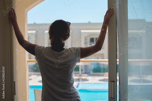 Woman standing near window on the hotel balcony and gazing on swimming pool © Lazy_Bear
