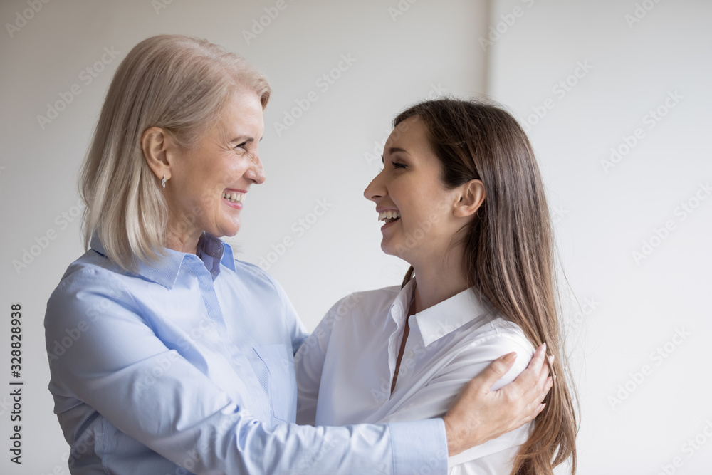 Happy mature mom and adult daughter hug show love and care at home, smiling senior mother and grown-up girl child embrace cuddle, enjoy weekend leisure time together, family bonding concept Happy mature mom and adult daughter hug show love and care at home, smiling senior mother and grown-up girl child embrace cuddle, enjoy weekend leisure time together, family bonding concept