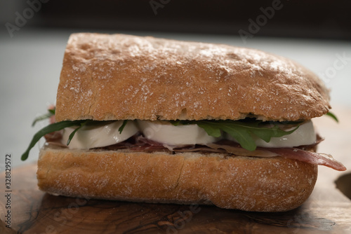 Sandwich with prosciutto, mozzarella and arugula on olive wooden board