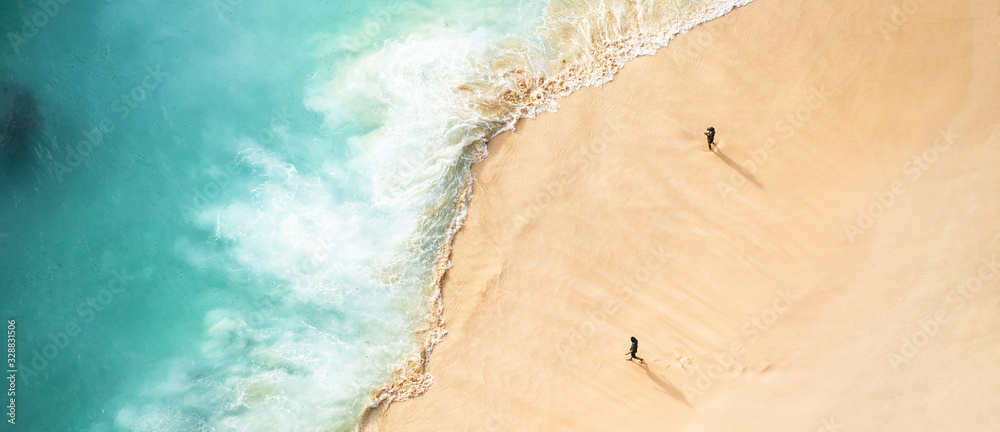 View from above, stunning aerial view of two people walking on a beautiful beach bathed by a turquoise sea during sunset. Kelingking beach, Nusa Penida, Indonesia.