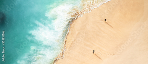 Obraz na płótnie View from above, stunning aerial view of two people walking on a beautiful beach bathed by a turquoise sea during sunset. Kelingking beach, Nusa Penida, Indonesia. w salonie