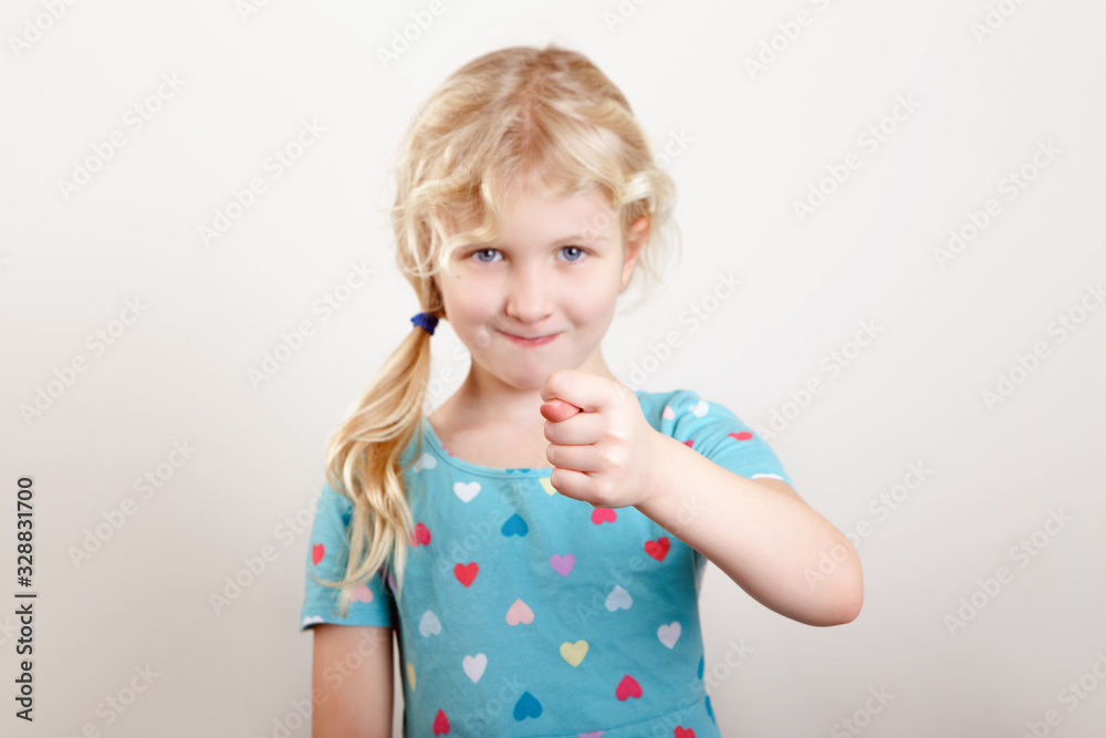 Child girl showing fig sign. Kid expressing strong negative emotion. Cute adorable blonde Caucasian preschool girl posing in studio on a light background. Child girl showing fig sign. Kid expressing strong negative emotion. Cute adorable blonde Caucasian preschool girl posing in studio on a light background.