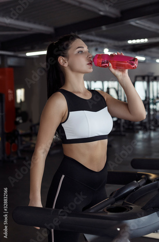 Fit young girl drinking water on treadmill in gym