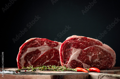 Raw rib eye beef steak with pepper and herbs on a wooden background in a butcher shop photo