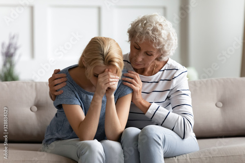 Loving senior mother sit on couch hug depressed millennial daughter suffering from breakup or divorce, caring mature mom embrace comfort upset grownup adult girl child, show support and understanding