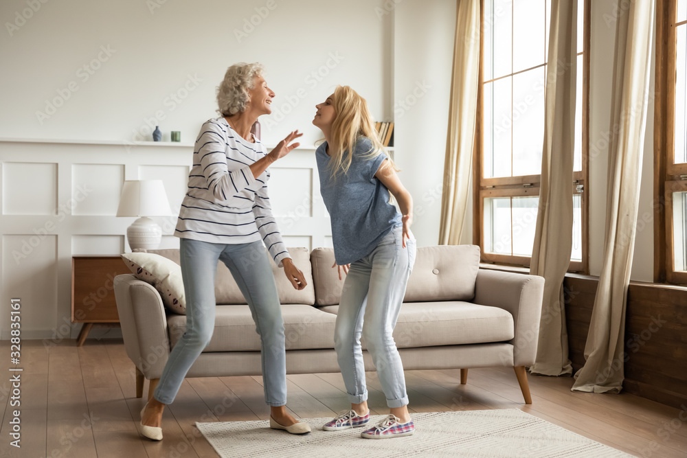 Overjoyed mature mother and millennial grownup girl child feel optimistic dancing together in living room, happy senior mom and adult daughter have fun engaged in funny activity, relaxing at home Overjoyed mature mother and millennial grownup girl child feel optimistic dancing together in living room, happy senior mom and adult daughter have fun engaged in funny activity, relaxing at home