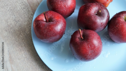 red ripe apples in drops of water on a blue dish on a wooden table 