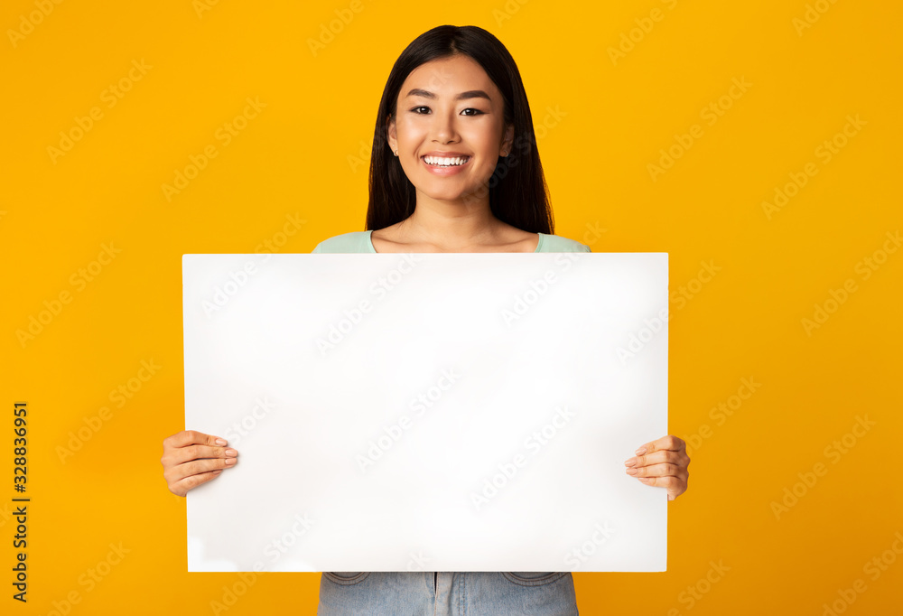 Asian Woman Holding Empty White Poster Standing On Yellow Background Asian Woman Holding Empty White Poster Standing On Yellow Background