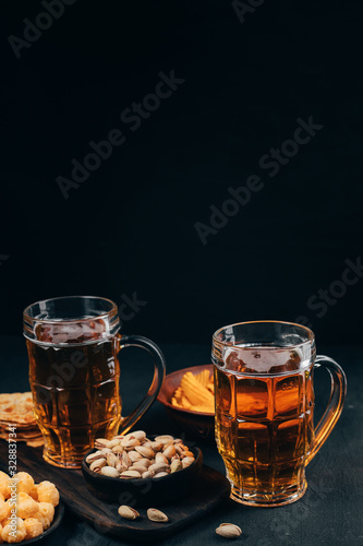 Appetizing salty beer snacks. Two mugs of craft lager, chips and pistachios. Oktoberfest food, pub concept