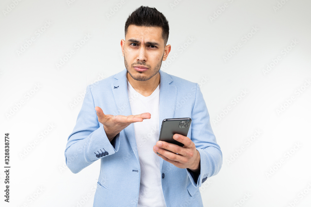 stylish brunette man in a blue classic jacket looks carefully at a smartphone on a white background
