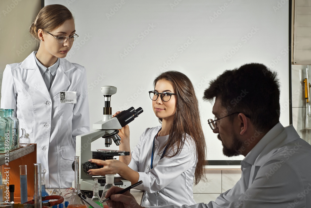 Obraz premium Team of scientists working in the laboratory. Assistants conduct chemical experiments. Girl near the microscope makes blood tests.