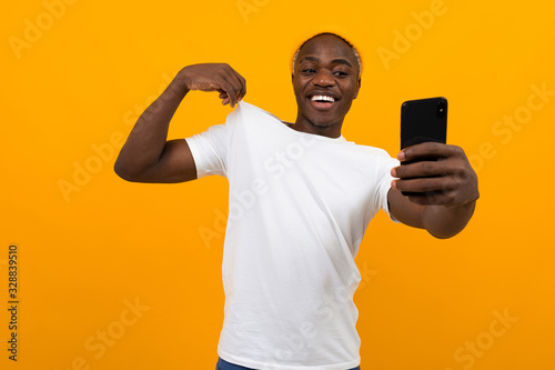 handsome black american man taking selfie on phone and smiling over orange background