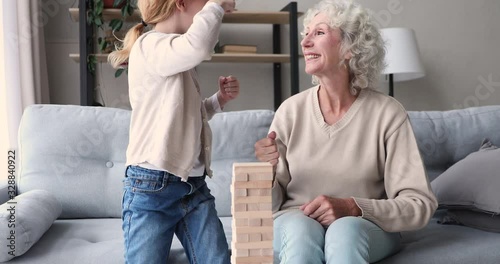 Happy senior grandma and cute kid granddaughter playing rock-paper-scissors hands jenga funny game at home. Two age generations family old grandparent and small grandkid enjoying activity together. photo