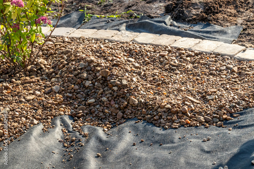Spreading river pebble over the laid woven geotextile fabric in the summer garden under reconstruction