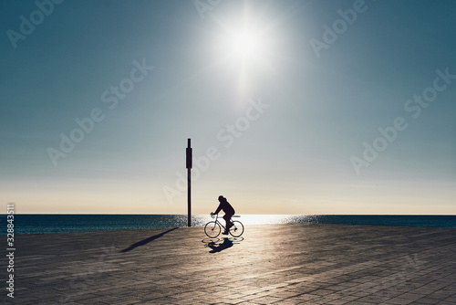 backlit silhouette of boy with a bicycle on the beach in barcelona photo