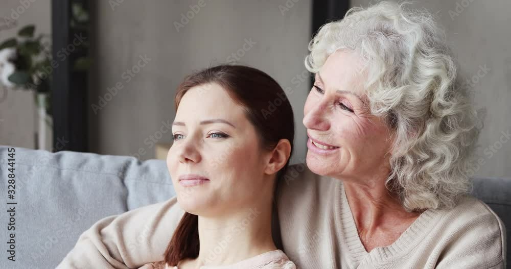 Relaxed loving senior mother embracing young daughter and talking resting on sofa. Happy old grandma bonding with adult granddaughter chatting enjoying moments of understanding and warm relationship. Relaxed loving senior mother embracing young daughter and talking resting on sofa. Happy old grandma bonding with adult granddaughter chatting enjoying moments of understanding and warm relationship.