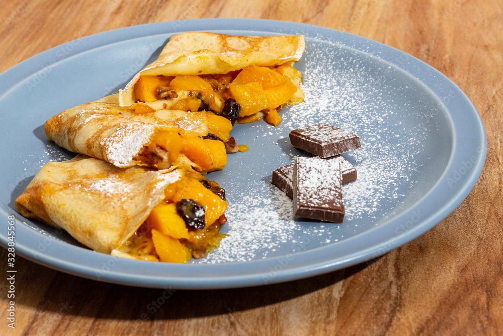 Mango crepes, with 3 chocolate feet, on a blue plate on a wooden table