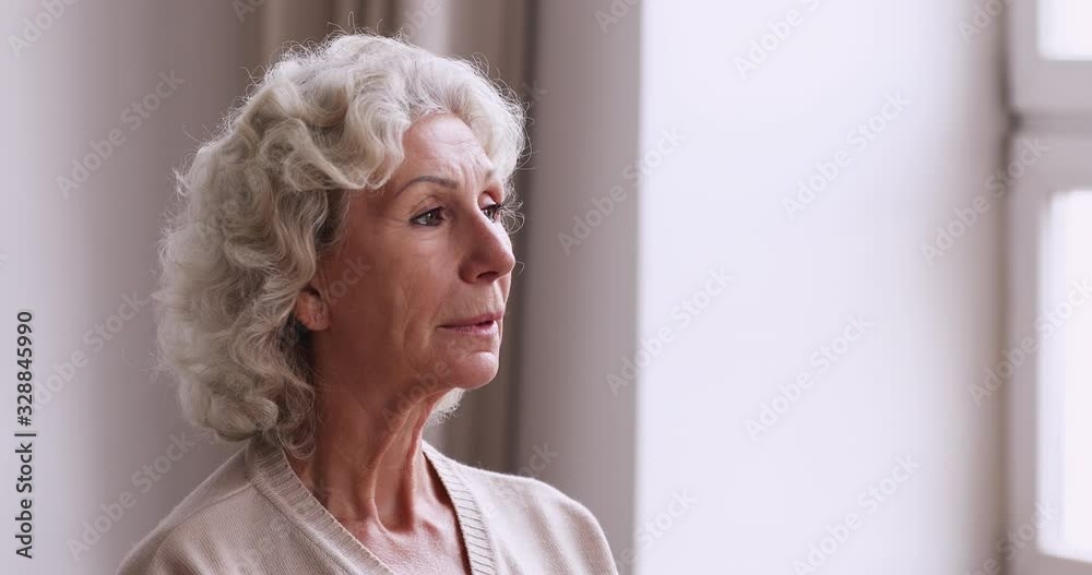 Sad pensive senior adult grandmother standing alone looking through window. Thoughtful abandoned old elder woman thinking of loneliness. Lonely melancholic 70s lady feeling solitude, remembering Sad pensive senior adult grandmother standing alone looking through window. Thoughtful abandoned old elder woman thinking of loneliness. Lonely melancholic 70s lady feeling solitude, remembering
