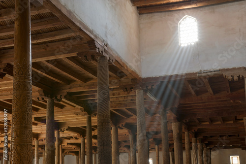 Main hall of Juma mosque (10th and 18th centuries) with old wooden pillars and sunbeams from the window. Khiva, Uzbekistan, Central Asia.