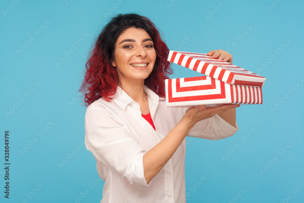 In anticipation of surprise. Portrait of attractive hipster woman with fancy red hair holding opened gift box and smiling to camera, satisfied with birthday present. indoor studio shot blue background In anticipation of surprise. Portrait of attractive hipster woman with fancy red hair holding opened gift box and smiling to camera, satisfied with birthday present. indoor studio shot blue background