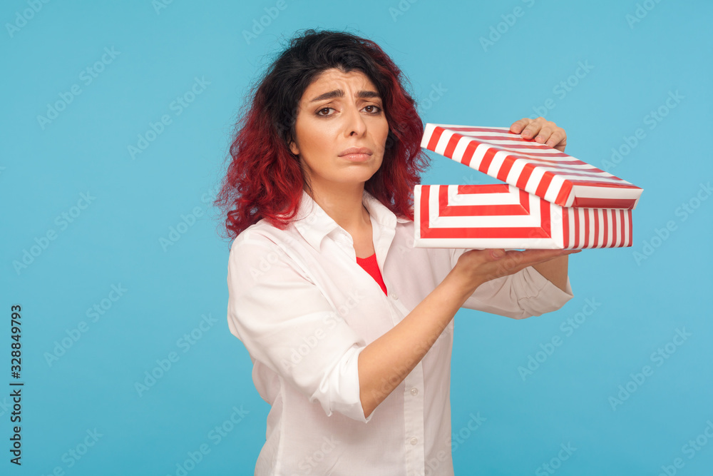 Bad present. Portrait of displeased unhappy woman with fancy red hair holding unpacked gift box and looking at camera with frustrated dissatisfied expression. studio shot isolated on blue background Bad present. Portrait of displeased unhappy woman with fancy red hair holding unpacked gift box and looking at camera with frustrated dissatisfied expression. studio shot isolated on blue background
