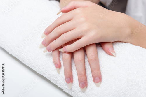 Woman holds hands on towel for manicure treatment procedure in spa salon. Beautiful hands of young woman close-up on towel. Spa treatments for nails. Space for text.